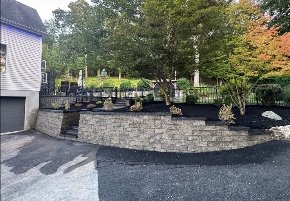 Stylish landscaped yard with stone retaining wall, black mulch, and colorful plants.