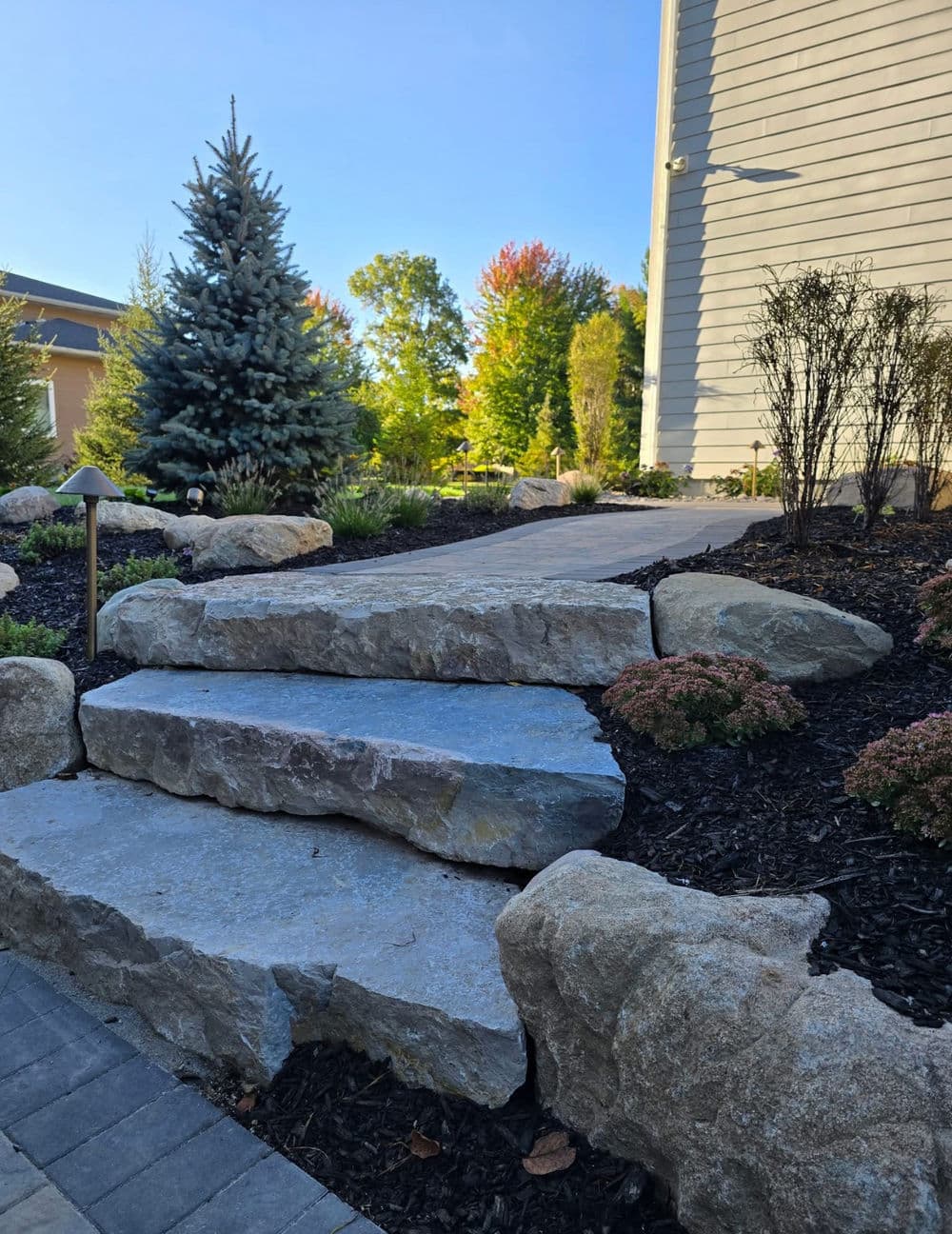 Stone pathway leading to a house with landscaped garden and evergreen trees.