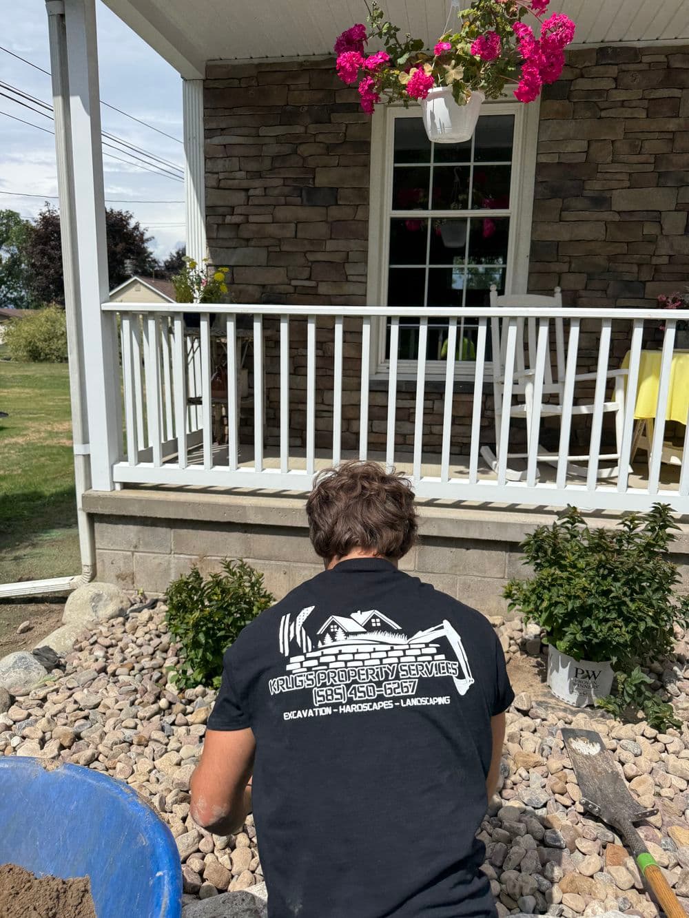 Landscaper working on a stone garden bed near a porch with pink flowers.