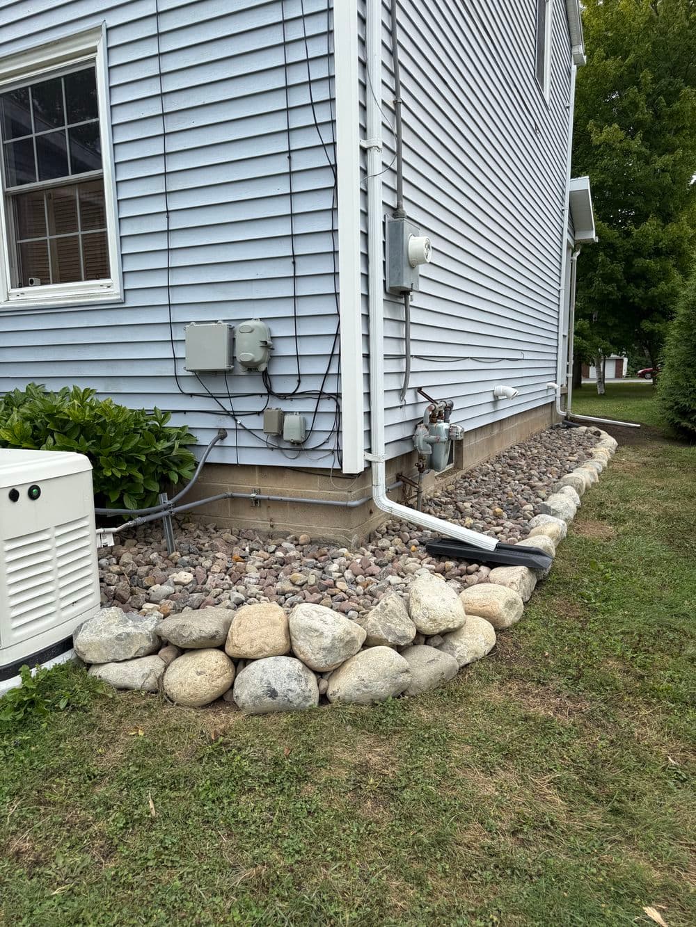 Stone landscape border along a blue house, featuring utility meters and greenery.